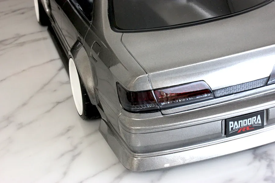 Rear corner view of a silver RC drift car body shell featuring tinted tail lights and a Pandora RC license plate on a marble surface.