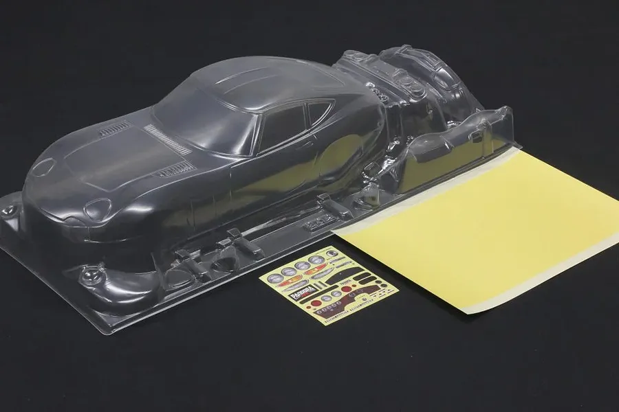 Unpainted clear polycarbonate Pandora RC Toyota 2000GT body shell with a mask sheet and sticker sheet on a black background.