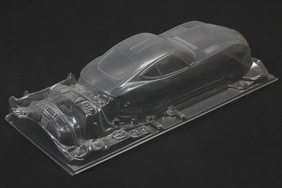 Unpainted clear polycarbonate RC car body shell for a Toyota 2000GT with separate molded detail parts on a dark background.