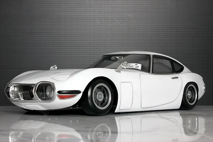 Studio shot of a white Pandora RC Toyota 2000GT body shell mounted on an RC chassis against a dark grey background.