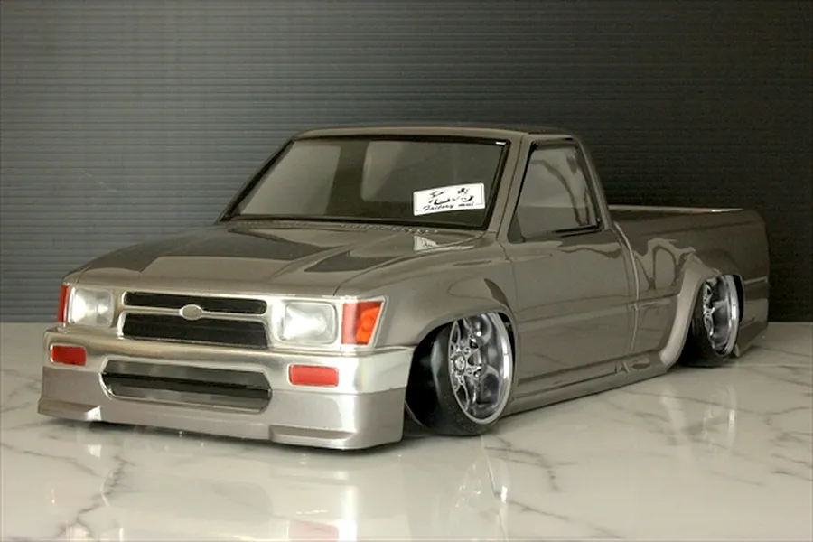 Pandora RC Toyota Hilux RN80 RC drift body shell painted metallic grey with wide fenders and custom wheels on a marble surface.