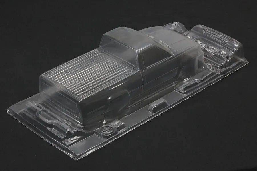Unpainted clear polycarbonate RC truck body shell for Toyota Hilux with separate accessories on a dark background.
