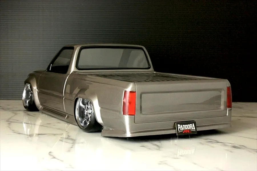 Rear-three-quarter view of a customized silver RC pickup truck body shell with lowered stance, custom wheels, and Pandora RC license plate.
