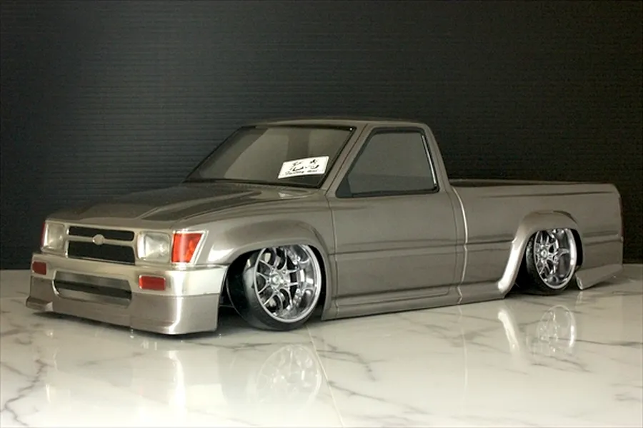 Silver painted Toyota Hilux RC drift truck body shell on a reflective marble surface against a dark background.