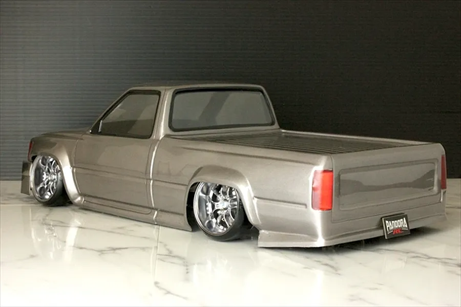 Rear-three-quarter studio view of a grey Pandora RC Toyota Hilux body shell mounted on a lowered chassis with chrome wheels.