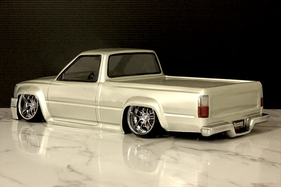 Silver RC pickup truck body shell displayed from a rear three-quarter angle on a marble surface.