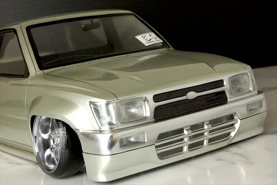 Close-up front angle of the painted silver Toyota Hilux RN80 RC body shell with custom wheels and a lowered stance.
