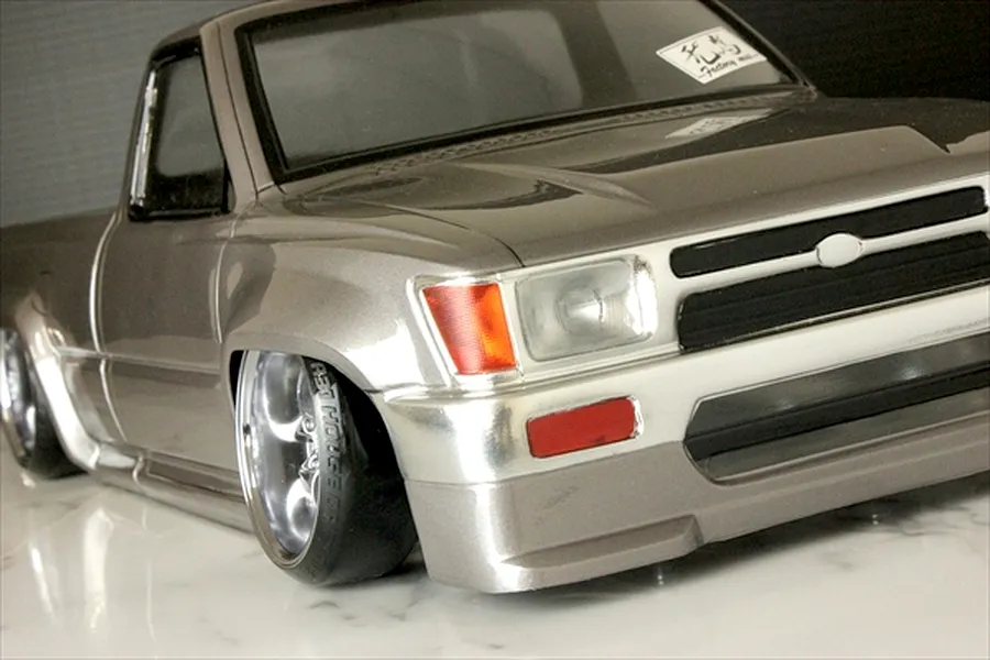 Close-up front angle of a custom silver RC drift truck body shell on a reflective surface.