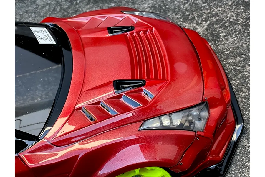 Close-up of the red painted bonnet and front fender vents on a Pandora RC body shell, outdoor setting.