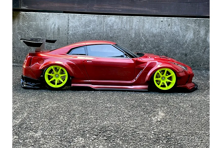 Side profile of a red Nissan GT-R RC drift car body with bright yellow wheels and a large rear wing on asphalt.