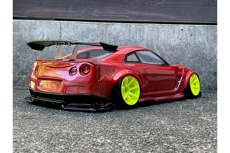 Red RC drift car body featuring a large rear wing and bright yellow wheels, parked on asphalt.
