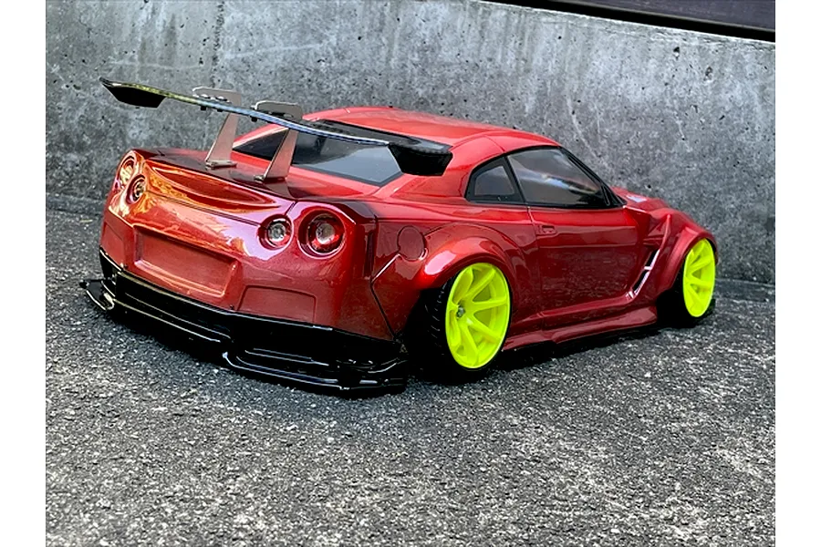 Rear three-quarter view of a metallic red RC drift car body shell on a Nissan GT-R chassis with bright yellow wheels and a large rear wing.