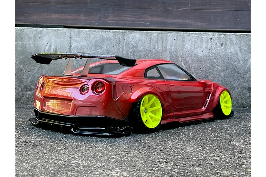 Rear three-quarter view of a painted red RC drift car body on a concrete surface with bright yellow rims and a large rear wing.