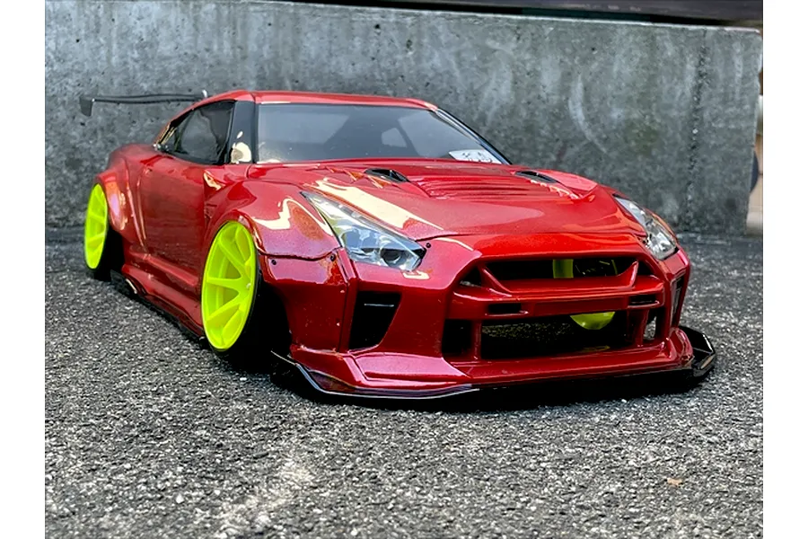 Custom painted red RC drift car body on an R35 GT-R with bright yellow wheels, parked on asphalt.
