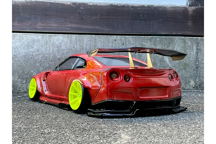 Rear three-quarter view of a red RC drift car with bright yellow wheels and a large rear spoiler parked on asphalt outdoors.