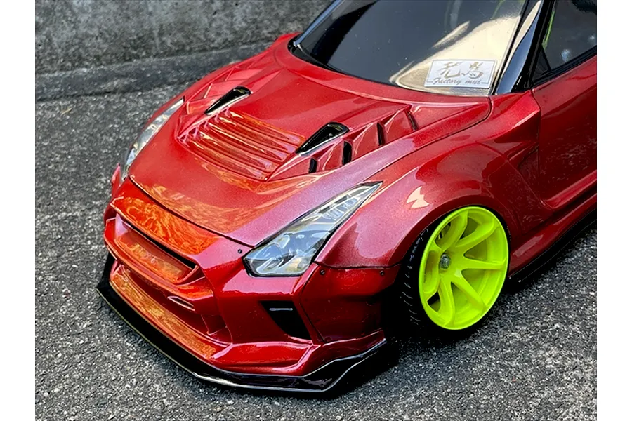 Close-up of a metallic red RC car body shell with bright green wheels on asphalt background.