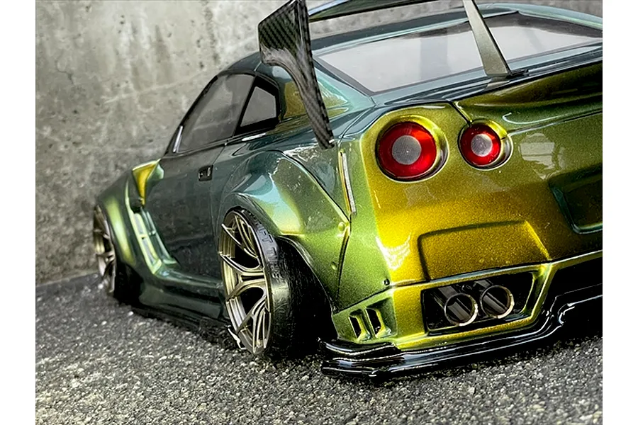 Rear-three-quarter view of a custom painted Nissan GT-R RC drift car body with wide body kit, large rear wing, and gold-to-green chameleon paint.
