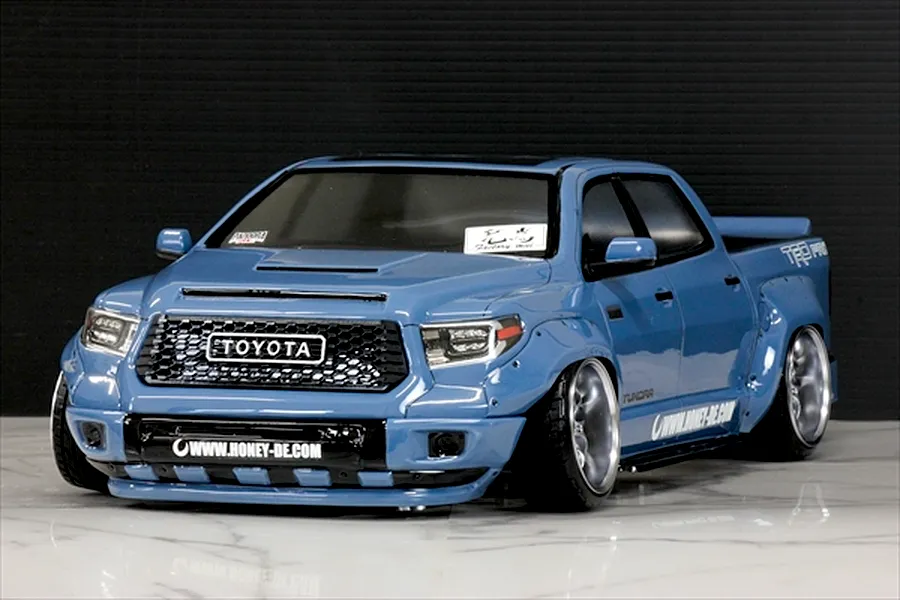 Blue Toyota Tundra RC truck body shell mounted on an RC chassis with wide fenders and custom wheels against a dark background.