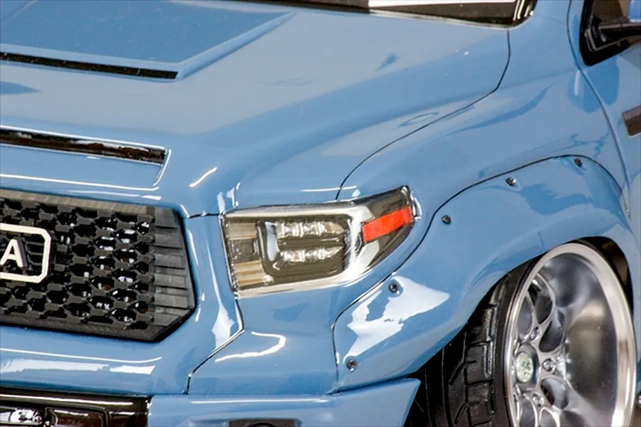Close-up of the front left quarter of a blue Toyota Tundra RC body shell, showing the headlight, grille, wide fender flare, and custom wheel.