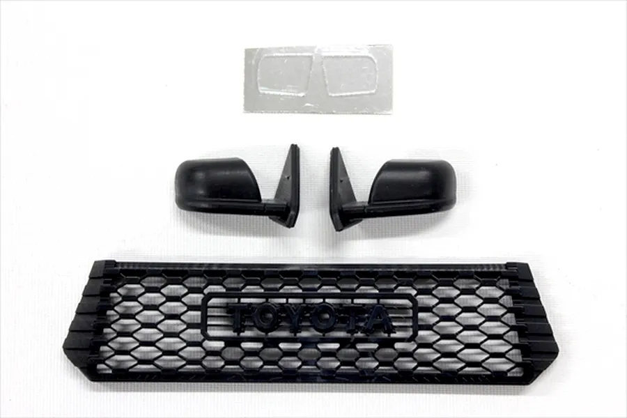 Black plastic RC scale accessories including a front grille with Toyota lettering, side mirrors, and a small decal sheet.