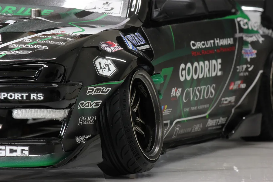 Close-up of the front wheel and fender of a black and green Pandora RC S14 Silvia drift car body with sponsor decals.