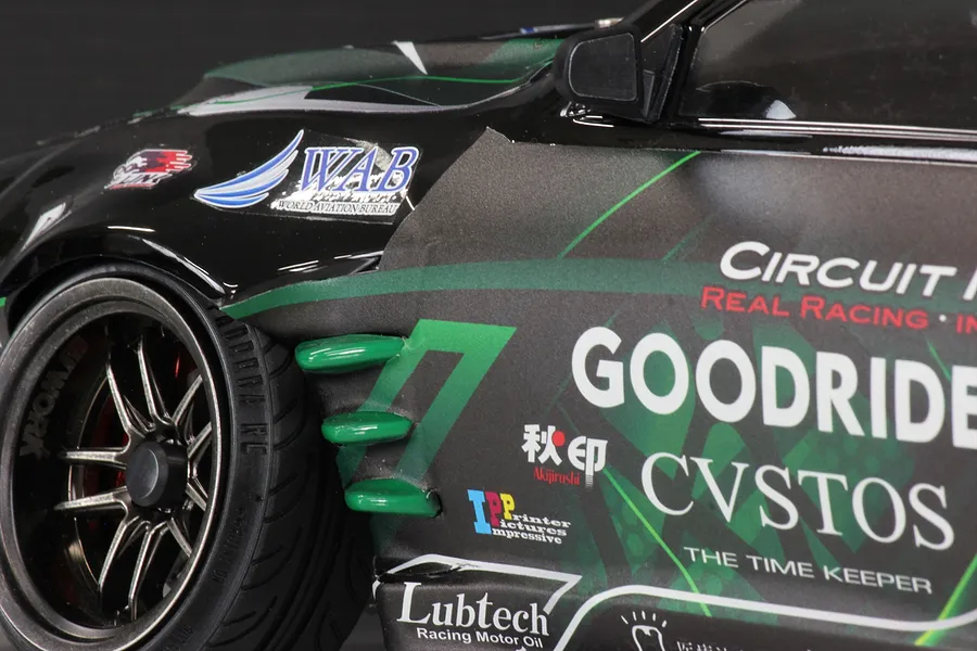 Close-up of the front fender and wheel of a black and green Pandora RC S14 Silvia RC drift car body with sponsor decals.
