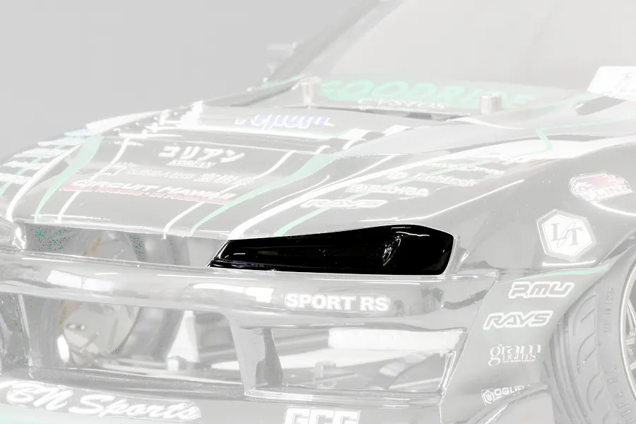 Close-up of a black RC car headlight bucket installed on a detailed model car body with sponsor decals.
