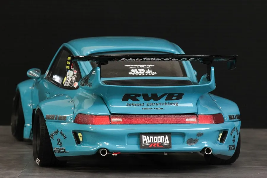 Rear three-quarter view of a light blue Pandora RC RWB 993 Type body shell with wide fenders, spoiler, and decals on a dark studio background.