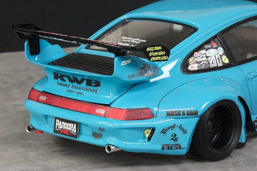 Close-up rear angle of a light blue Pandora RC RWB 993 type body shell featuring a large black wing, exhaust tips, and sponsor decals.