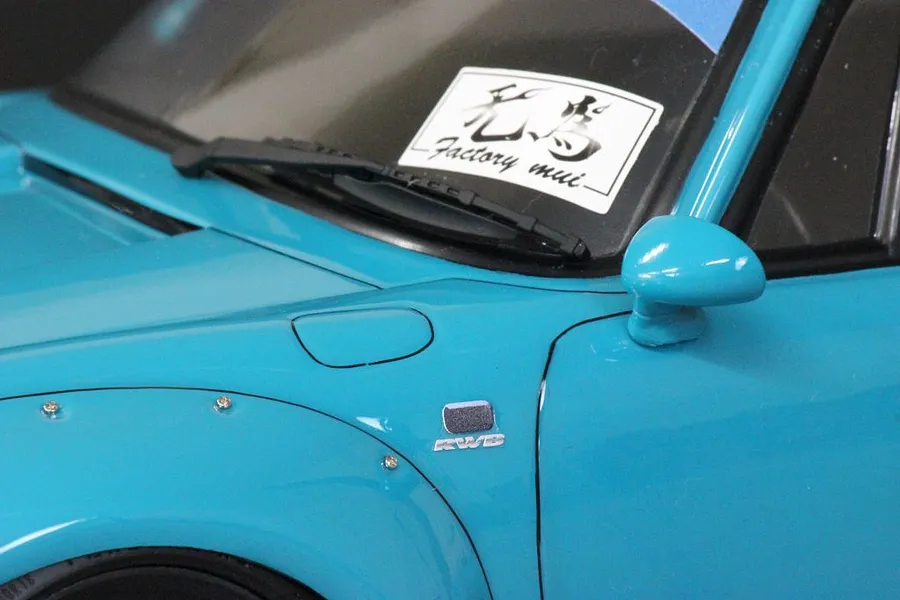 Close-up of a blue RC car body shell showing the front fender, side mirror, wiper, and RWB branding.