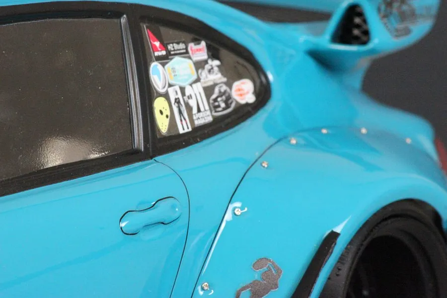 Close-up of a blue RC car body shell showing side window decals and a wide fender arch with visible hardware.