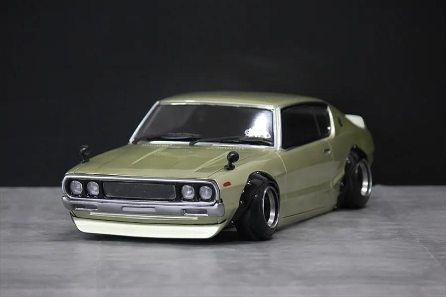 Front three-quarter view of a gold Pandora RC KPGC110 Skyline 2000GT-R drift car body shell on a grey surface.