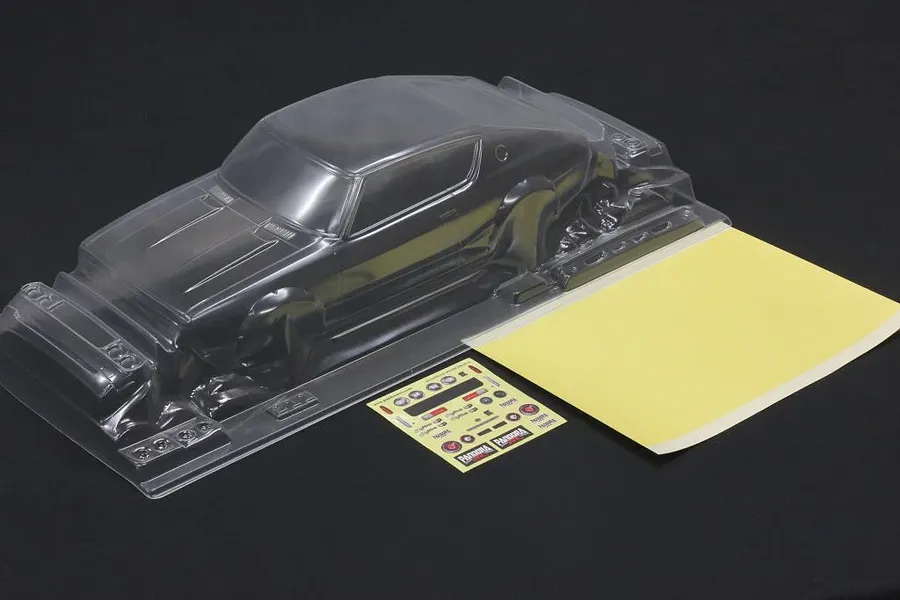 Unpainted clear polycarbonate RC car body shell with a sticker sheet and masking sheet on a black surface.
