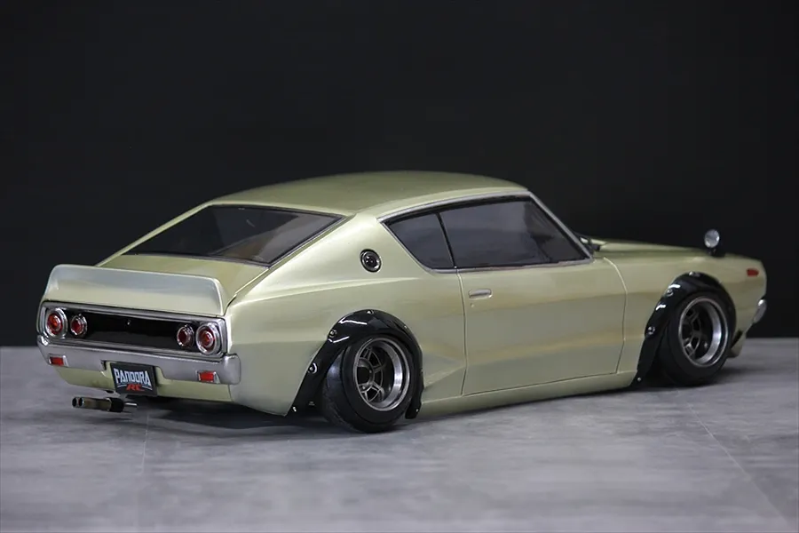 Rear three-quarter view of a gold Pandora RC KPGC110 Skyline 2000GT-R drift car body shell on a grey surface.