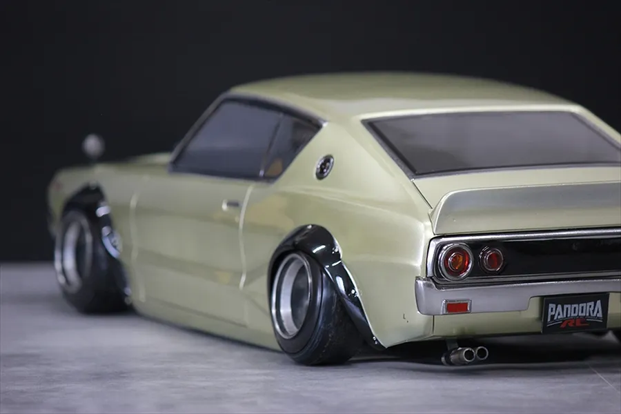 Rear-three-quarter studio view of a gold Pandora RC KPGC110 Skyline 2000GT-R drift car body shell with fender flares.