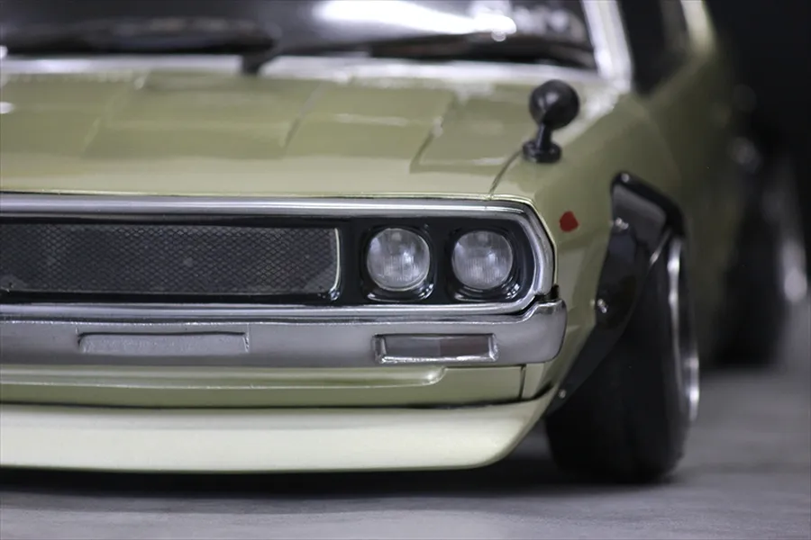 Close-up of the front left corner of a light green KPGC110 Skyline RC car body shell, showing grille, dual headlights, bumper, and fender flare.