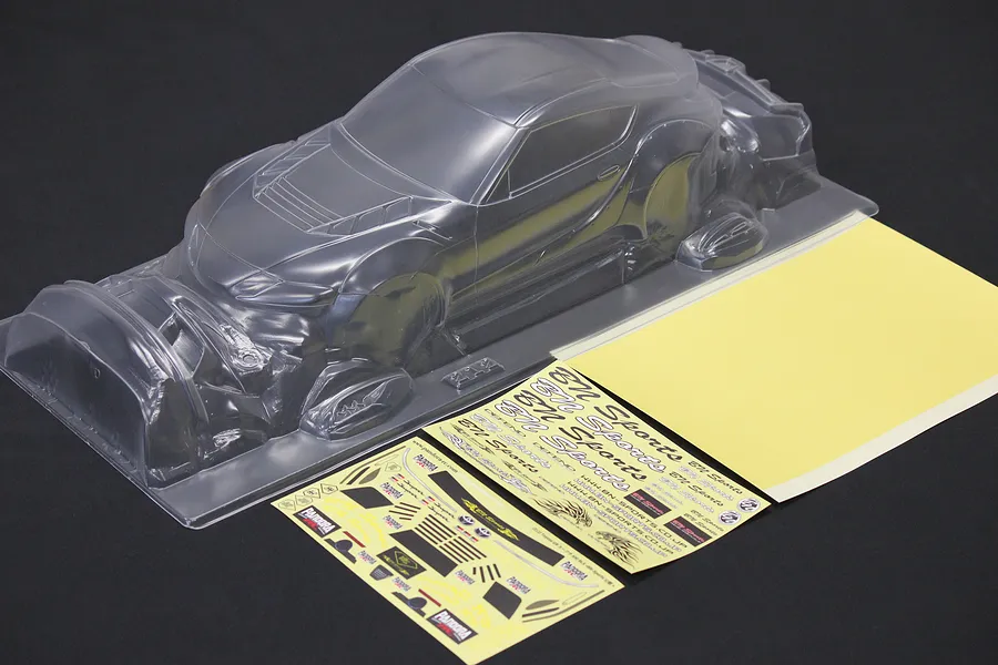 Unpainted clear polycarbonate RC car body shell with separate decal sheets on a dark surface.
