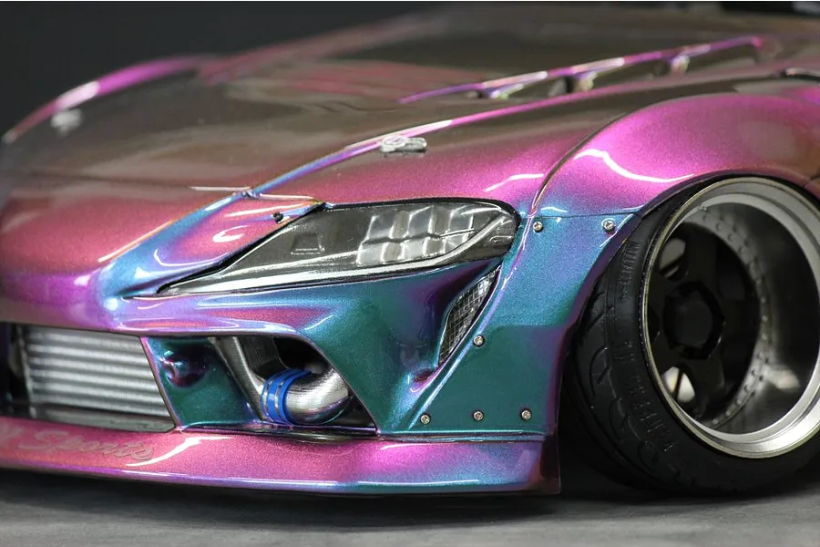 Close-up of the front corner of a colour-shifting purple and turquoise RC drift car body showing headlights and front wheel.