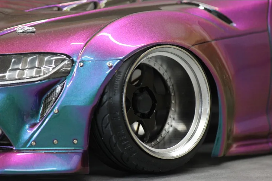 Close-up view of the front wheel and iridescent purple and blue wide body kit on a Toyota GR Supra A90 RC drift car body.