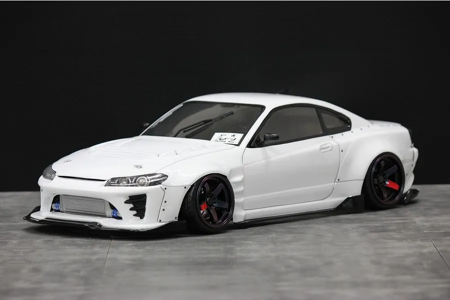 Painted white RC drift car body shell mounted on a chassis, featuring wide fenders, front intercooler, and black wheels against a dark background.