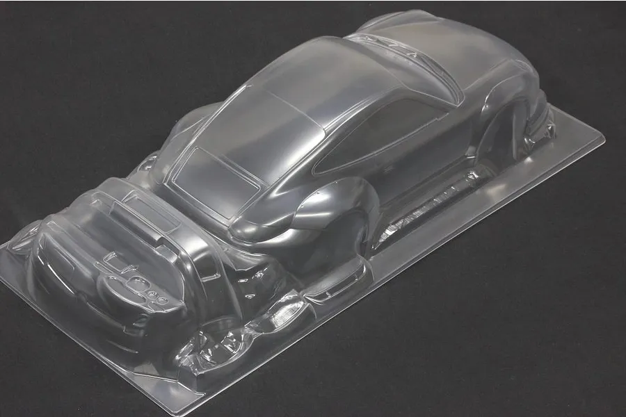 An unpainted, clear polycarbonate RC car body shell of a sports car shown from a high-angle view on a dark background.
