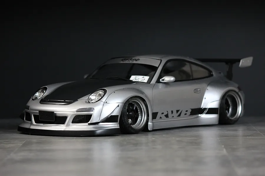 Silver RWB 997 RC drift car body shell mounted on a chassis with wide fenders, black hood, and RWB side graphics against a dark background.