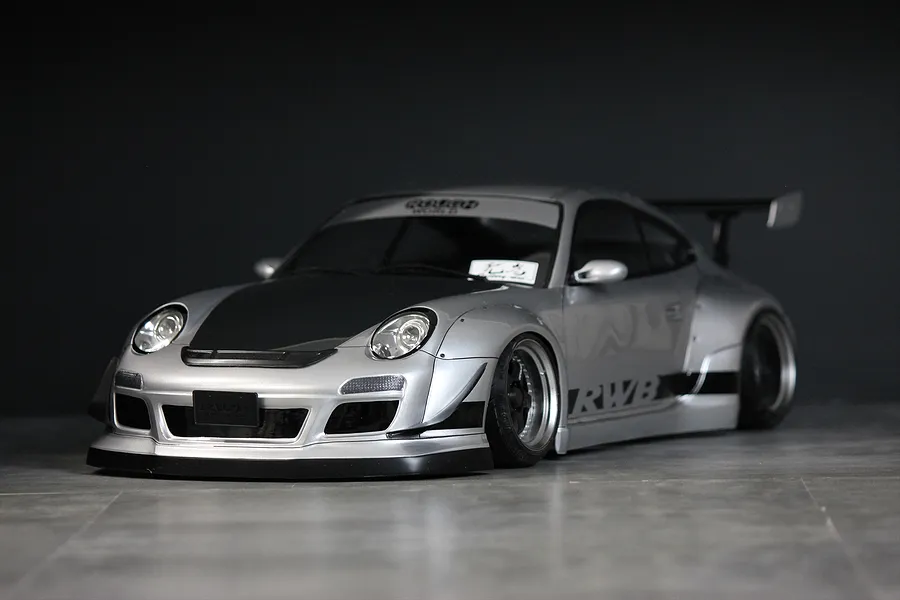 Silver Pandora RC RWB 997 Type drift body shell mounted on an RC chassis with wide fenders, black bonnet, and wing against a dark backdrop.