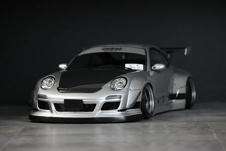 Silver RWB 997 RC drift car body shell with black hood, wide fenders, and rear wing on a dark background.