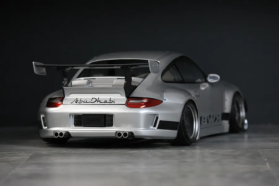 Rear three-quarter view of a silver RWB 997 RC body shell with a large rear wing, quad exhaust tips, and Abu Dhabi branding.