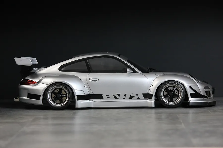Side profile of a silver Pandora RC RWB 997 Type drift body shell with a large rear wing and black accents on a dark background.