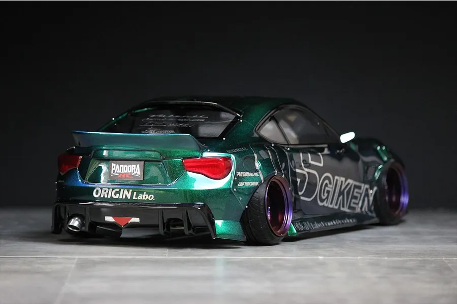 Rear-three-quarter angle view of a custom metallic green RC drift car body shell, featuring wide fenders, sponsors decals, and deep-dish wheels.