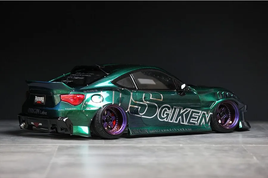 Rear-three-quarter view of a customized metallic green RC drift car body on a grey surface with a dark background.
