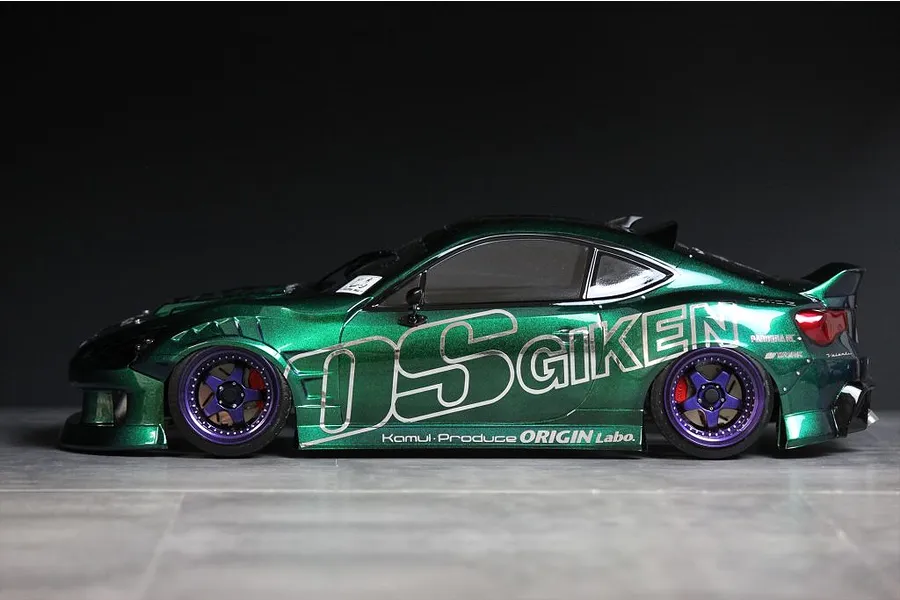 Side view of a metallic green RC drift car body shell mounted on a chassis with purple and black wheels against a dark background.