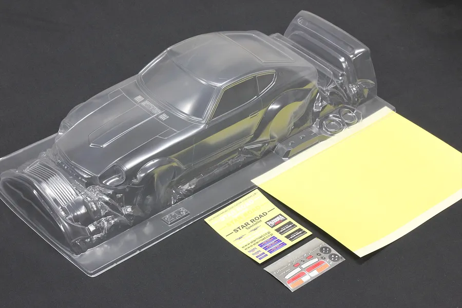 Unpainted clear polycarbonate Pandora RC S30 Fairlady Z body shell with decal sheets and masking film on a dark surface.